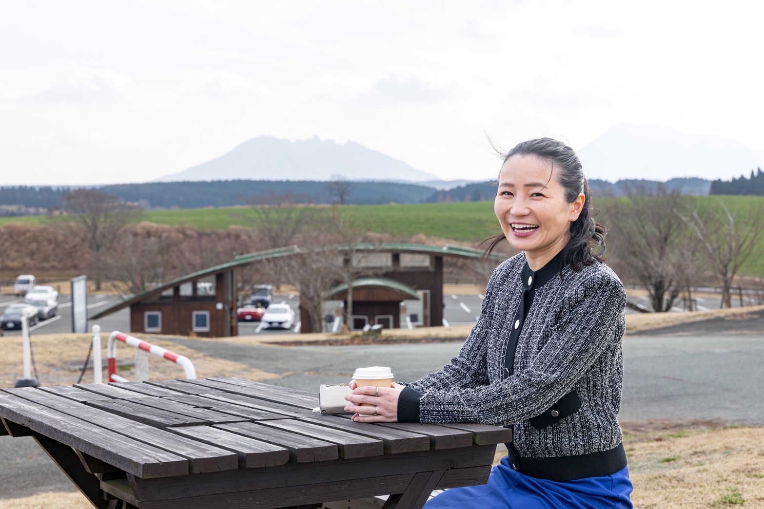 阿蘇の風景をバックに笑顔の田中三恵
